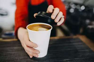 barista putting lid on cup of coffee to go