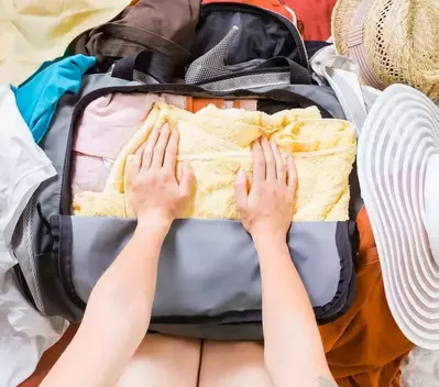 Top view of hands packing a suitcase full of clothes