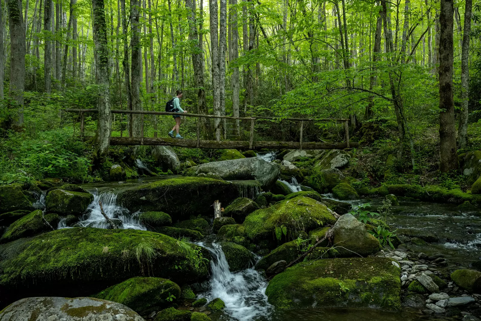 hiker crossing footbridge over mountain stream